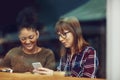 Lets text some friends to come hangout with us. two young friends looking at something on a cellphone in a cafe. Royalty Free Stock Photo