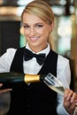 Lets toast to you. Attractive waitress pouring champagne into a champagne glass smiling at the camera. Royalty Free Stock Photo