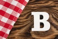 Letter B of the alphabet - Red checkered cloth tablecloth on rustic wood background. Text space Royalty Free Stock Photo
