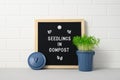 Letter board with text SEEDLINGS IN COMPOST and miniature trash container with seedling growing against white brick wall
