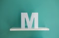 Letter M turquoise color on a white shelf