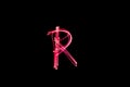 Letter R written with light paint photography technique on black background.