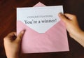 A letter that says Congratulations You`re a winner! with hands holding a pink envelope