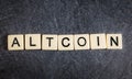 Letter tiles on black slate background spelling Altcoin