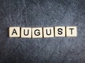 Letter tiles on black slate background spelling August