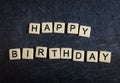 Letter tiles on black slate background spelling happy birthday