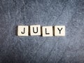 Letter tiles on black slate background spelling July