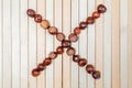 Letter X or multiplication sign is laid out with ripe large chestnuts in close up on light wooden background. Flat lay