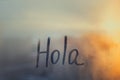 lettering Hola in Spanish language is Hello in english on foggy glass on sunset window