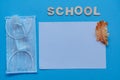 Lettering School on a blue background with a white sheet, dry oak leaf, sanitizer and mask on blue flatley. New academic year.