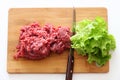 Lettuce salad and ground beef on a cutting board with a knife between them. Plant-based meat concept.