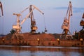 Level-luffing bulk-handling cranes load sand onto a barge in a river port in the evening light