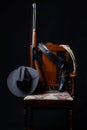 Lever action rifle, revolver, rope, cowboy hat and a chair with a black background Royalty Free Stock Photo
