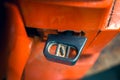The lever of the air suction cable for cold starting the engine on the body of an orange chainsaw close-up. Rich-fuel mixture