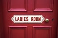 Old vintage metal painted sign saying Ladies Room on a painted red wooden background with brass door handle Royalty Free Stock Photo