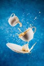 Levitating cup, saucer and creamer with splashing plant-based milk and coffee on blue Royalty Free Stock Photo