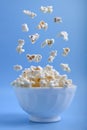 Levitating levitation falling popcorn in a white ceramic bowl and around it on blue background . Side view