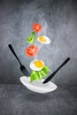 Levitating scrambled egg, sliced tomatoes, lettuce, plate, black fork and knife on gray background Royalty Free Stock Photo