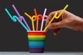 LGBT color cup with multi-colored cocktail tubes on a gray background. Male hand holds a straw for drinks. The concept of