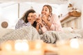 LGBT female couple having fun under a blanket on the sofa - Cute blonde Caucasian woman drink cup of tea in living room laughing Royalty Free Stock Photo