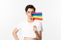 Lgbtq community. Attractive queer man with flitter on face, waving pride rainbow flag and looking at camera, standing in