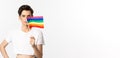 Lgbtq community. Attractive queer man with flitter on face, waving pride rainbow flag and looking at camera, standing in