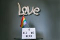 LGBTQ pride month background. A light box with the text Love is all we need under a silver foil balloon with a rainbow