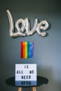 LGBTQ pride month background. A light box with the text Love is all we need under a silver foil balloon with a rainbow