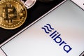 Libra the Facebook cryptocurrency logo on mobile phone screen and real coins of other crypto such as Bitcoin next to it