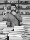 Librarian concept. Man on thoughtful face stands between piles of books, while holds hourglass, bookshelves on Royalty Free Stock Photo