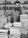 Librarian concept. Man on thoughtful face stands between piles of books, while studying in library, bookshelves on Royalty Free Stock Photo