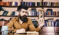 Library and librarian. Man on thoughtful face holds hourglass while studying, bookshelves on background. Teacher or Royalty Free Stock Photo