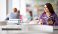 Pretty female student with laptop and books working in a high school library Royalty Free Stock Photo