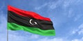 Libya flag on flagpole on blue sky background. Libyan flag fluttering in the wind against a background of sky with clouds. Place
