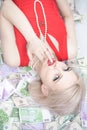 A beautiful blonde woman in a red dress is lying on a lot of money and enjoying life. rich caucasian girl top view
