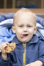 A licking baby with a cookie in his hand sitting in a stroller