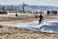 An athlete walks among the foam of the waves shore with his kite surfing board at Roman beach crowded by bathers and people Royalty Free Stock Photo