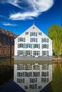 View over town moat on old medieval white house, sweeping willow tree, clear blue sky, symmetrical strong reflection in water Royalty Free Stock Photo