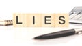 Lies word assembled from wooden cubes next to a calculator, pen and notepad