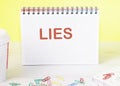 Lies the word is written on a blank sheet in a notebook standing on a table on a yellow background