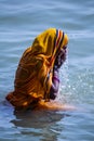 Life on the Ganges: woman in a bright yellow or orange sari bathing in the Ganges as religious ritual. beautiful color contrasts.
