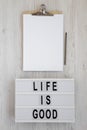 `Life is good` words on a lightbox, clipboard with blank sheet of paper on a white wooden background, top view. Overhead, from Royalty Free Stock Photo