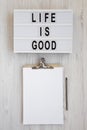 `Life is good` words on a modern board, clipboard with blank sheet of paper on a white wooden background, top view. Overhead, fr Royalty Free Stock Photo