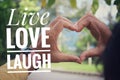 Life inspirational quote - Live love laugh. With person making heart sign with fingers, love symbol with hands on soft green park. Royalty Free Stock Photo