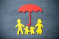 Life insurance concept. Paper cutout of family father, mother, son and daughter under red umbrella on blackboard background. Royalty Free Stock Photo