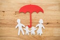 Life insurance concept. Paper cutout of family father, mother, son and daughter under red umbrella on wooden background. Royalty Free Stock Photo