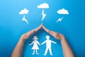 Life insurance and family health concept. Hands protect paper figures origami from lightning from the clouds on blue background