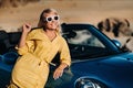 A life Portrait of a young woman enjoying a ride through a deserted valley, getting out of a convertible on the side of the road. Royalty Free Stock Photo