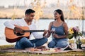 Life is a song, love is the music. a young man playing a guitar while on a picnic with his girlfriend at a lakeside. Royalty Free Stock Photo