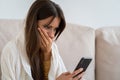 Life troubles, break up with boyfriend, bad news, heartbreak. Worried woman sitting on couch holds mobile phone read message